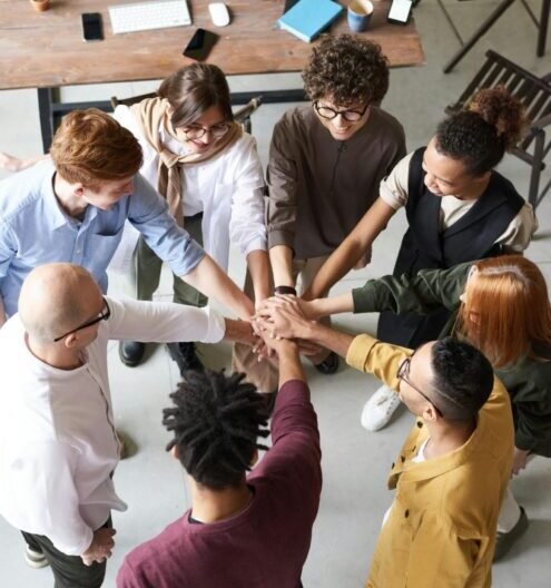 A diverse group of professionals joins hands in a team-building exercise indoors.